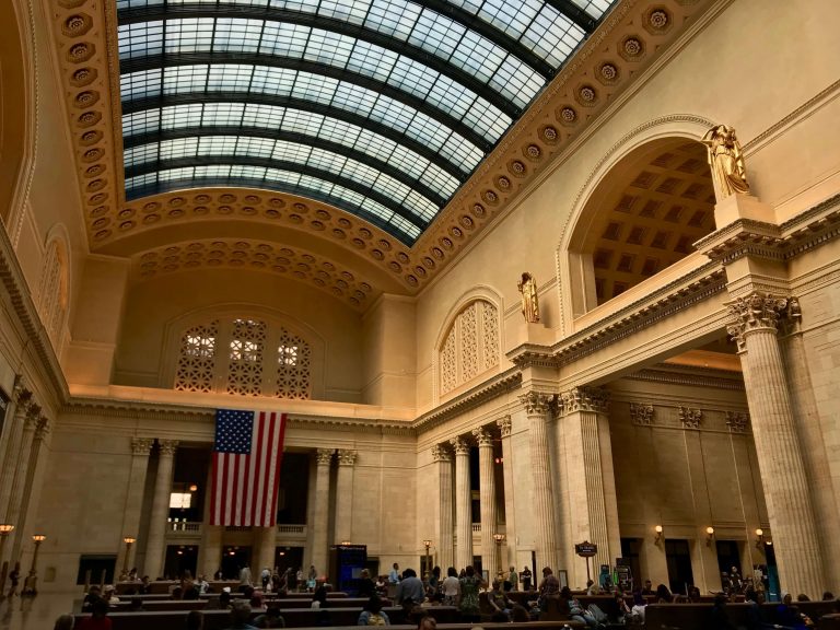 Towering columns and a US flag in the waiting room of Chicago's Union Station train depot, home to Amtrak passenger trains. ©KettiWilhelm2019