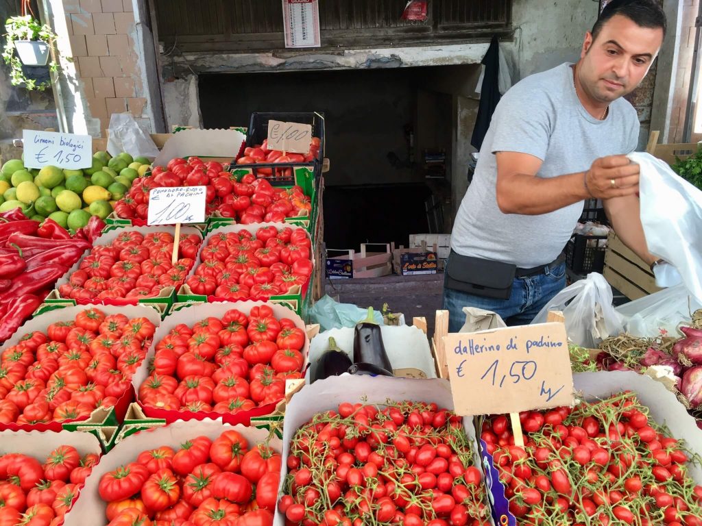 A man selling many varieties of tomatoes at market in Sicily. (Having a diet rich in vegetables is part of how Italians stay thin.) ©KettiWilhelm2017