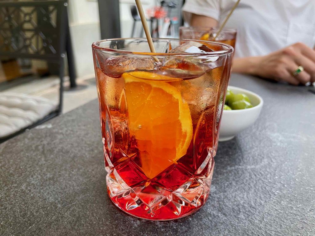 A bright red Americano cocktail – a classic Italian aperitivo drink – with a slice of orange on a table in Milano, Italy. ©KettiWilhelm2021