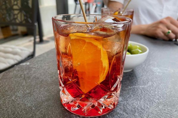 A bright red Americano cocktail – a classic Italian aperitivo drink – with a slice of orange on a table in Milano, Italy. ©KettiWilhelm2021