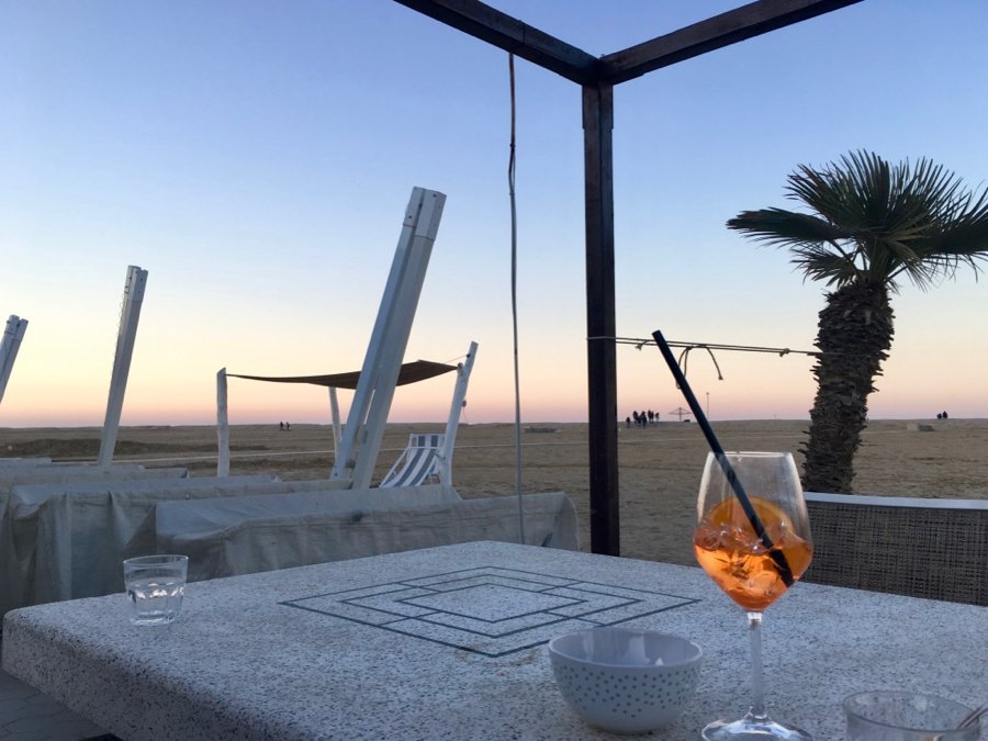A bright orange Italian cocktail – the famous Aperol Spritz – on a table in front of an empty beach in Rimini, Italy. ©KettiWilhelm