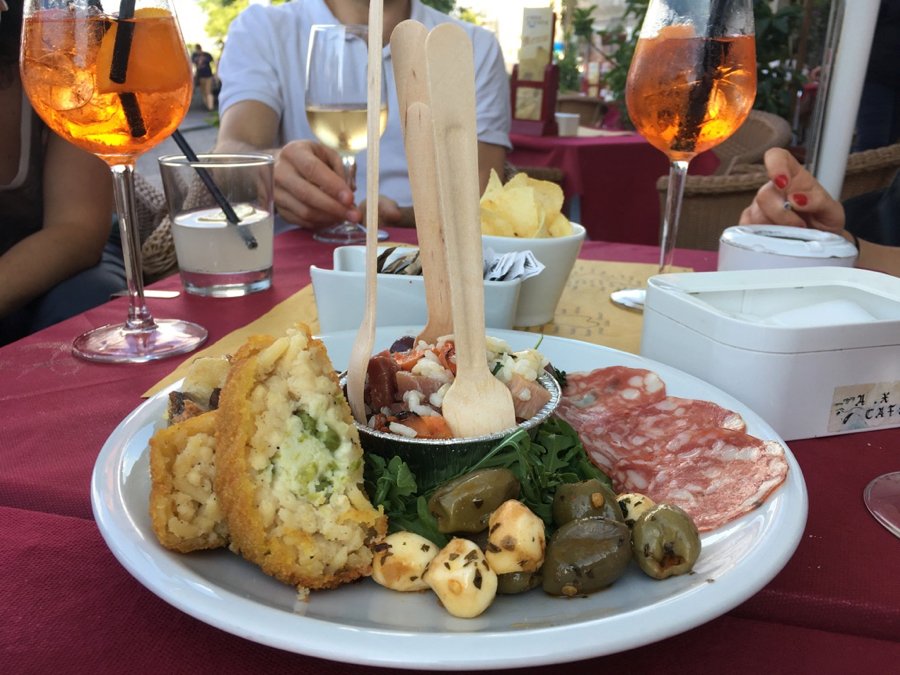 Aperitivo drinks and a typical aperitivo snack platter in Naples, Italy, to share with several people: Arancini, olives, cured meats, and a rice salad. ©KettiWilhelm2020
