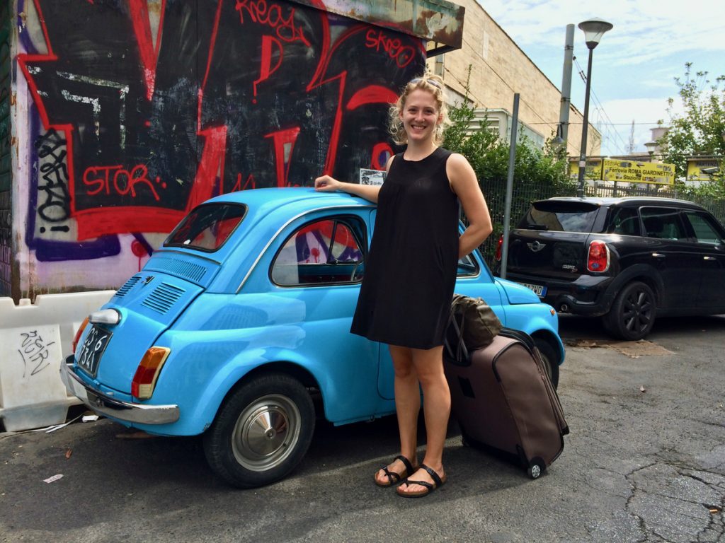 The author standing with her luggage in front of a small blue car in Rome, after moving to Italy to continue my expat travel blog. ©KettiWilhelm2016