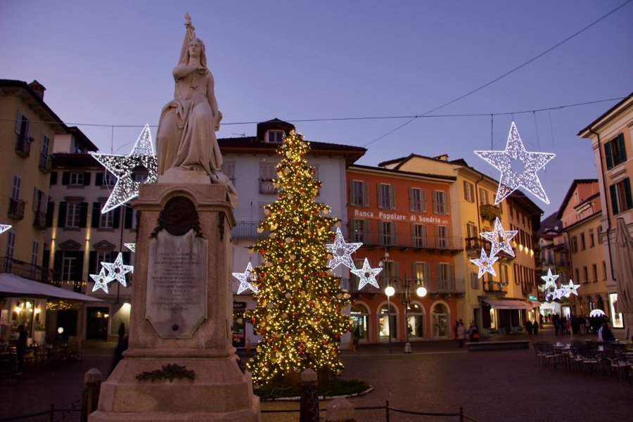 A statue, a Christmas tree, and lots of beautiful lights in a small town plaza at dusk in Italy. ©KettiWilhelm2020