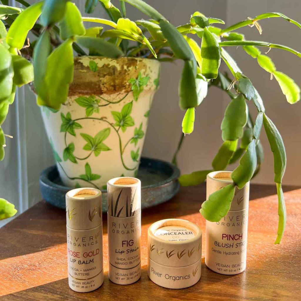 The reviewer's collection of toiletries from River Organics, all packaged in cardboard tubes, on a wooden desk in front of a house plant. ©KettiWilhelm2022