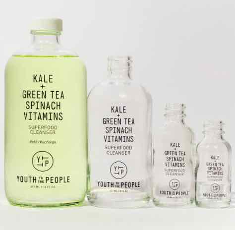 Four glass bottles of Youth To The People Superfood Cleanser (reviewed in this article). The largest bottle, on the left, is full of bright green face wash, while the other smaller refill sizes are empty. 