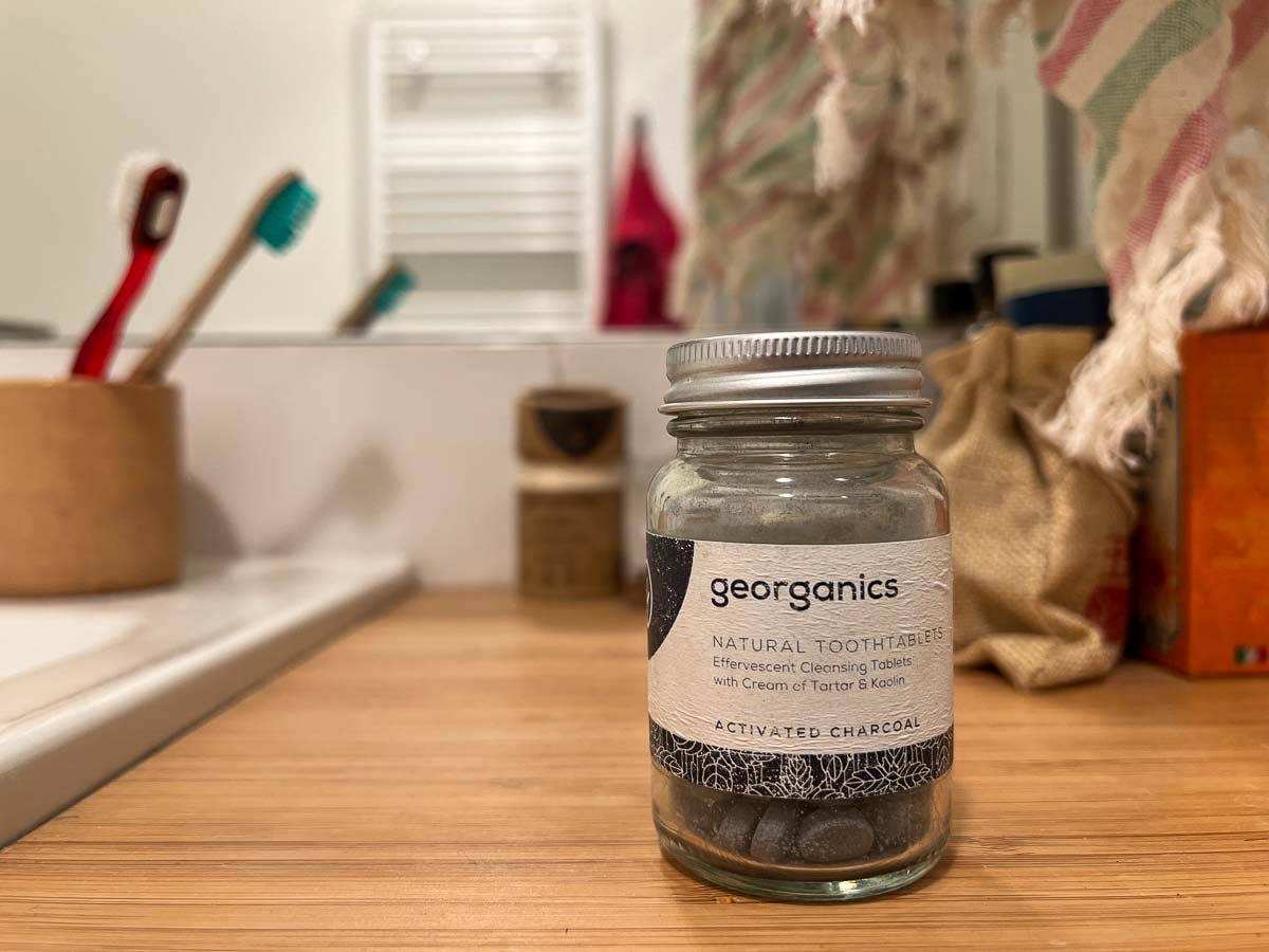 A glass bottle of charcoal toothpaste tablets from plastic-free brand Georganics sits on a wooden bathroom counter. ©KettiWilhelm2022