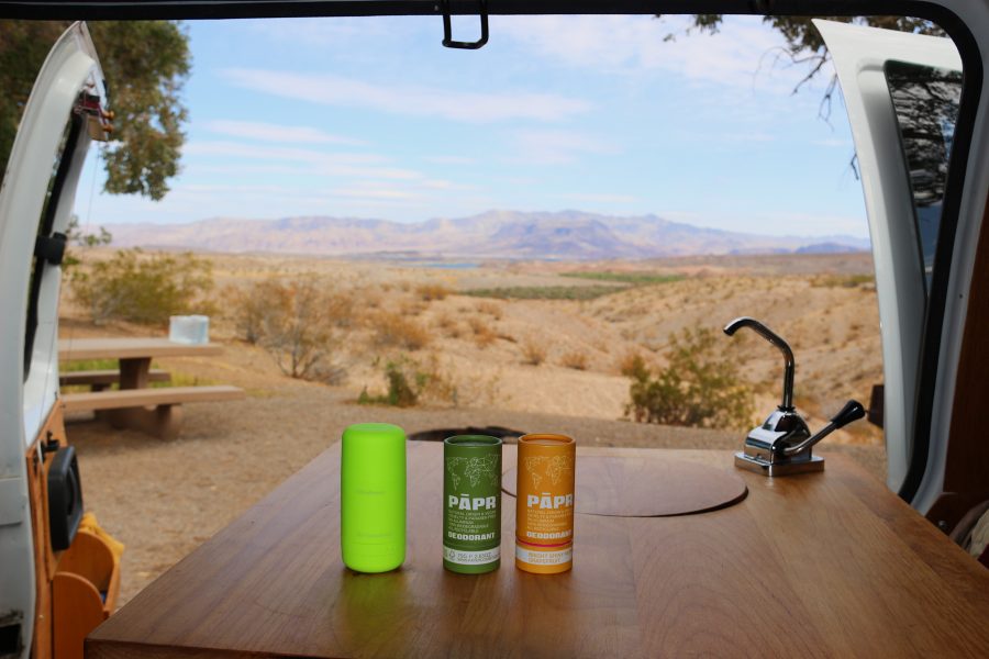 Three tubes of zero-waste deodorant (by the eco-friendly brands byHumankind and PAPR deodorant) on a wood table with a sink inside a camper van, with the Nevada desert behind them. ©KettiWilhelm2021