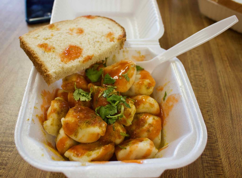 A dish of vegetarian Russian dumplings at Pel’meni, in downtown Juneau, topped with bright red curry, hot sauce, vinegar and green cilantro. Unfortunately, they’re served in Styrofoam and with a plastic fork. ©KettiWilhelm2021