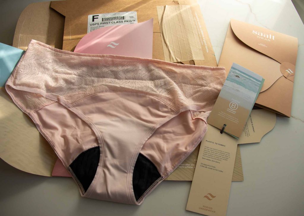 A pair of lacy, pink Saalt brand period underwear, an alternative to Thinx pictured with their plastic-free packaging. ©KettiWilhelm2022