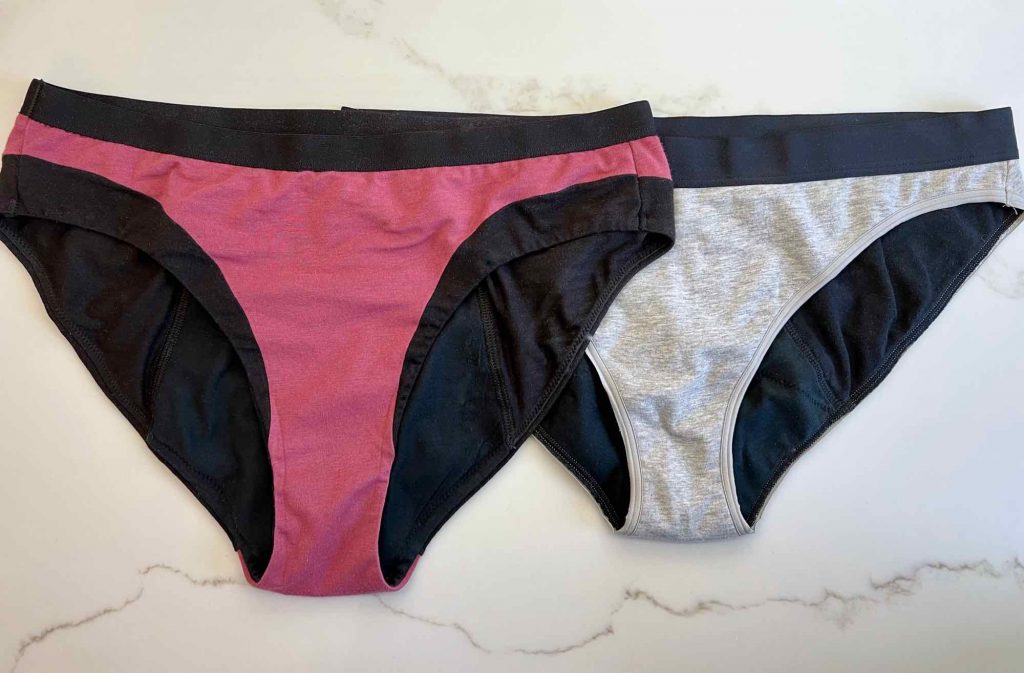 The new Thinx cotton modal style, in pink with black trim, overlapping the now discontinued Thinx organic cotton bikini, in gray. ©KettiWilhelm2021