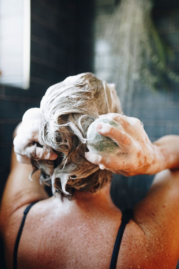 The head and shoulders of a white woman with blond hair in a shower lathering up her hair with an Earthling Co. shampoo bar – the brand’s rich lather is one reason I think they’re some of the best shampoo bars in this review.