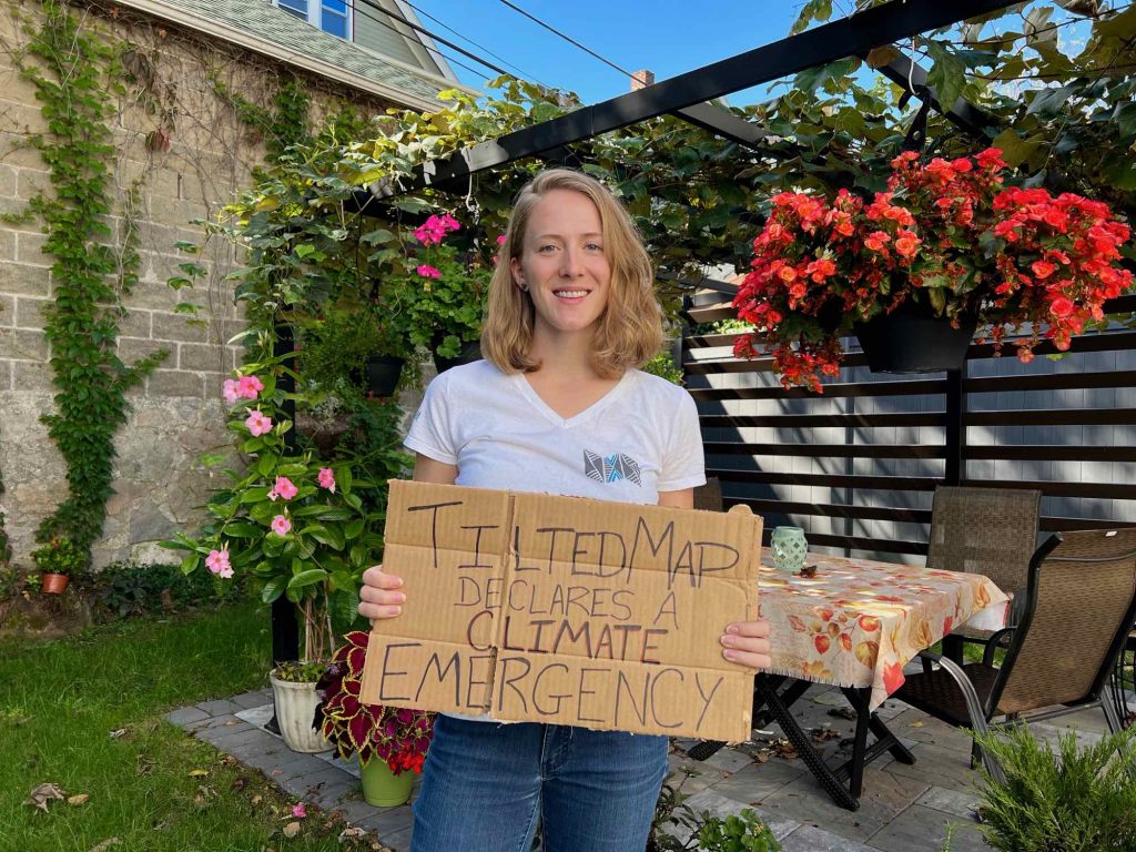 The author, sustainable travel blogger Ketti Wilhelm, holds a cardboard sign saying "Tilted Map declares a climate emergency," joining Tourism Declares. ©KettiWilhelm2021