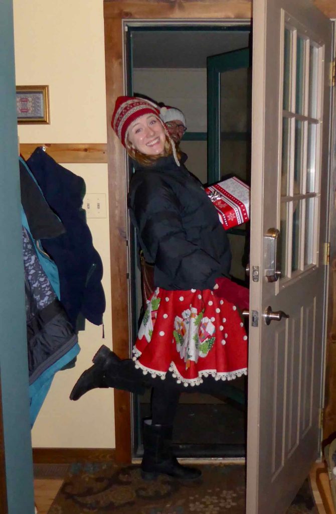 The author of this sustainable gift guide, in a doorway wearing a Christmas tree skirt as a real skirt, and carrying a wrapped present. ©KettiWilhelm2021
