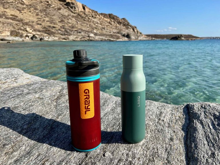 My LARQ self-cleaning water bottle, and Grayl filtering water bottle, sitting on a rock with the turquoise waters of the Mediterranean behind. ©KettiWilhelm2021