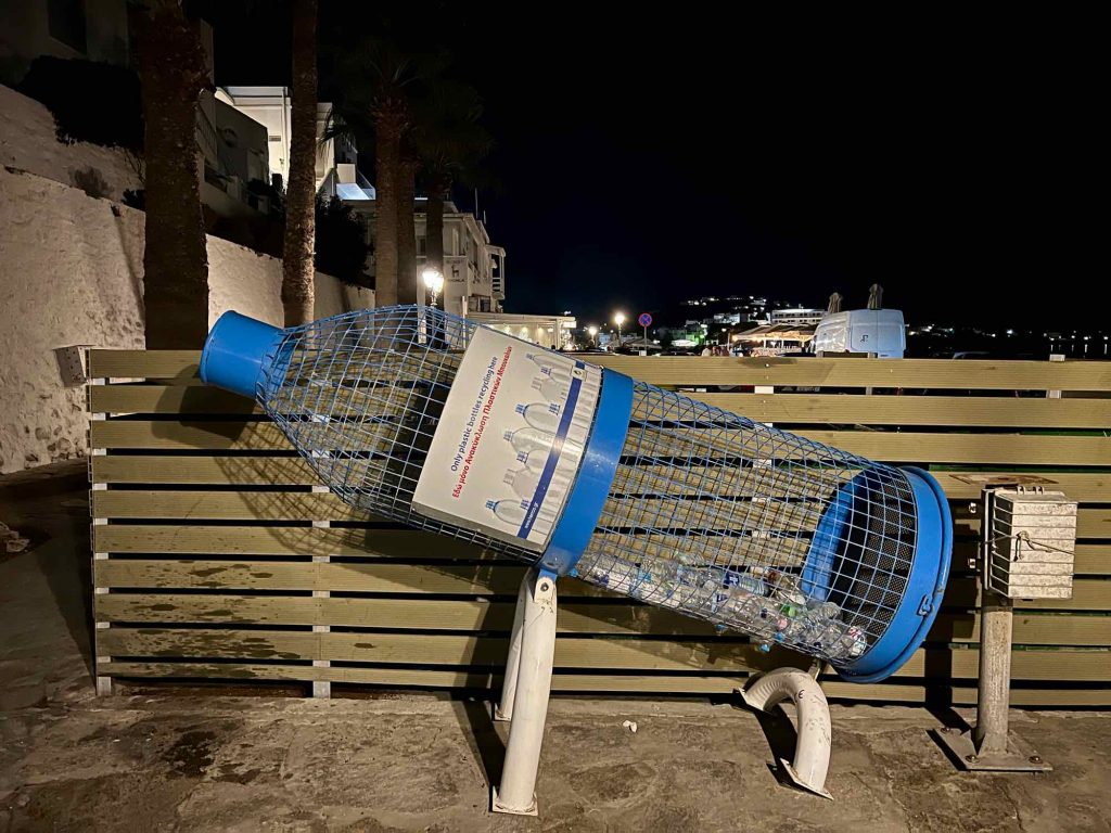 One of the initiatives of Clean Blue Paros: A bottle-shaped recycling collection bin made of wire for PET plastic bottles, near the beach on the Greek island of Paros. ©KettiWIlhelm2021