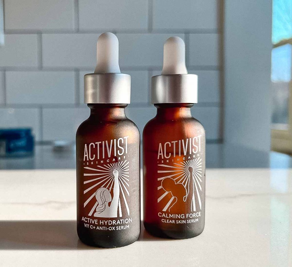 Brown glass refillable bottles of Activist Skincare's two serums – Calming Force and Active Hydration – sitting on a white marble counter top in front of a white tile backdrop. ©KettiWilhelm2022