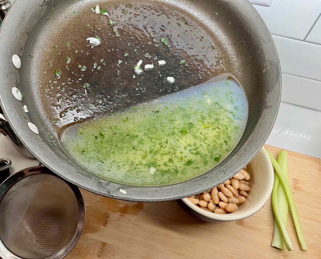 A pan tilted to show a mixture of water, garlic and parsley, where the mussels were steamed for this pasta recipe. ©KettiWilhelm2022