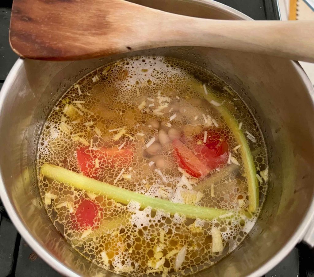 Looking down into a pan with white beans, celery sticks, cherry tomatoes and garlic, with the water saves from steaming the mussels. ©KettiWilhelm2022