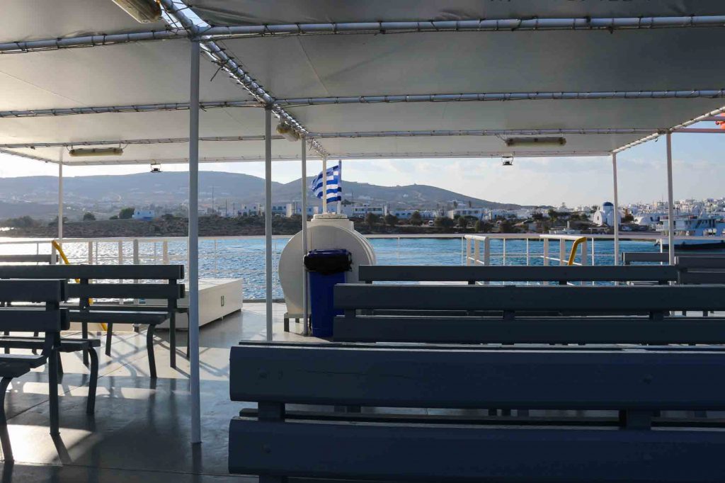 A nearly empty ferry traveling from Antiparos to Paros, Greece. Empty ferry seats in the foreground, and the island of Paros in the background, bathed in late afternoon lights. ©KettiWilhelm2022
