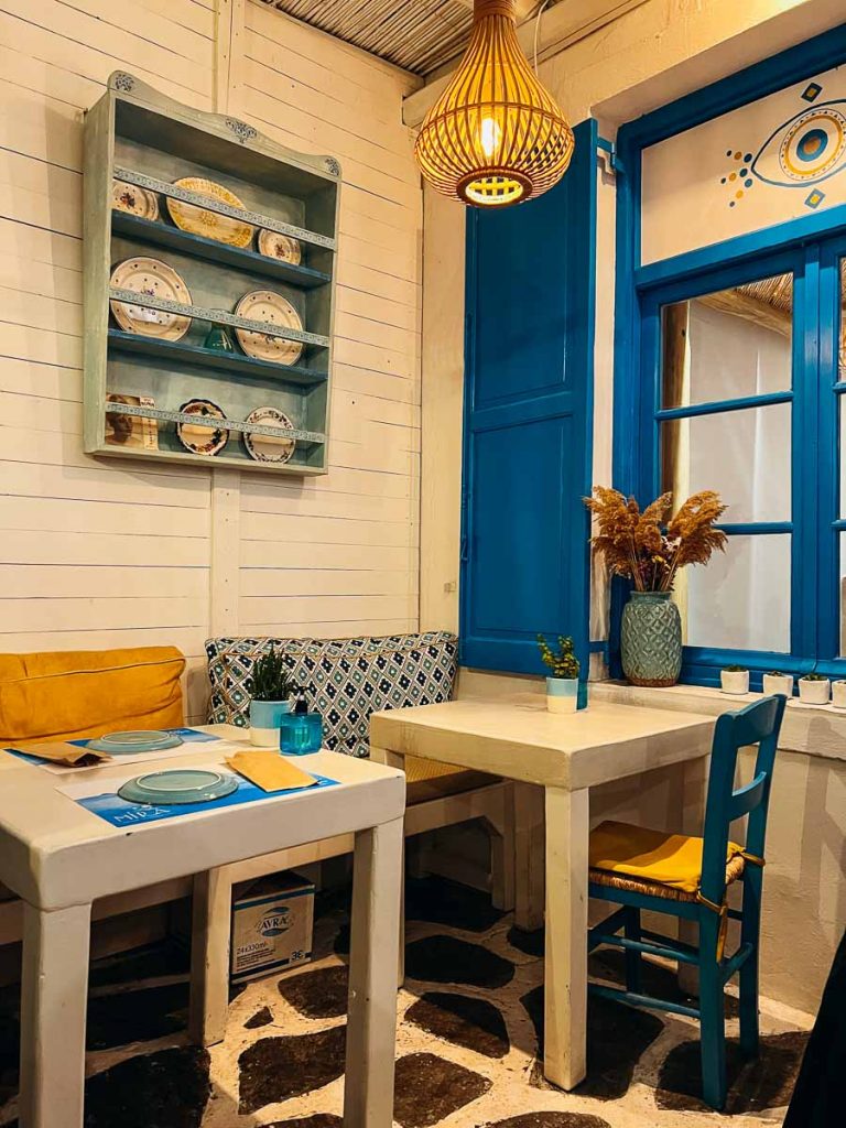 A cozy table for two in the corner at Mira Restaurant, with warm yellow light and classic Greek blue decorations. ©KettiWilhelm2022