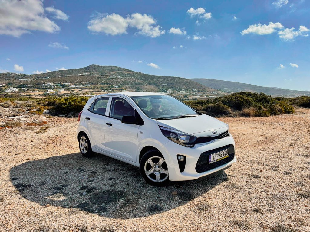A white rental car sitting on a natural gravel area with the mountains of Paros in the background. ©KettiWilhelm2022