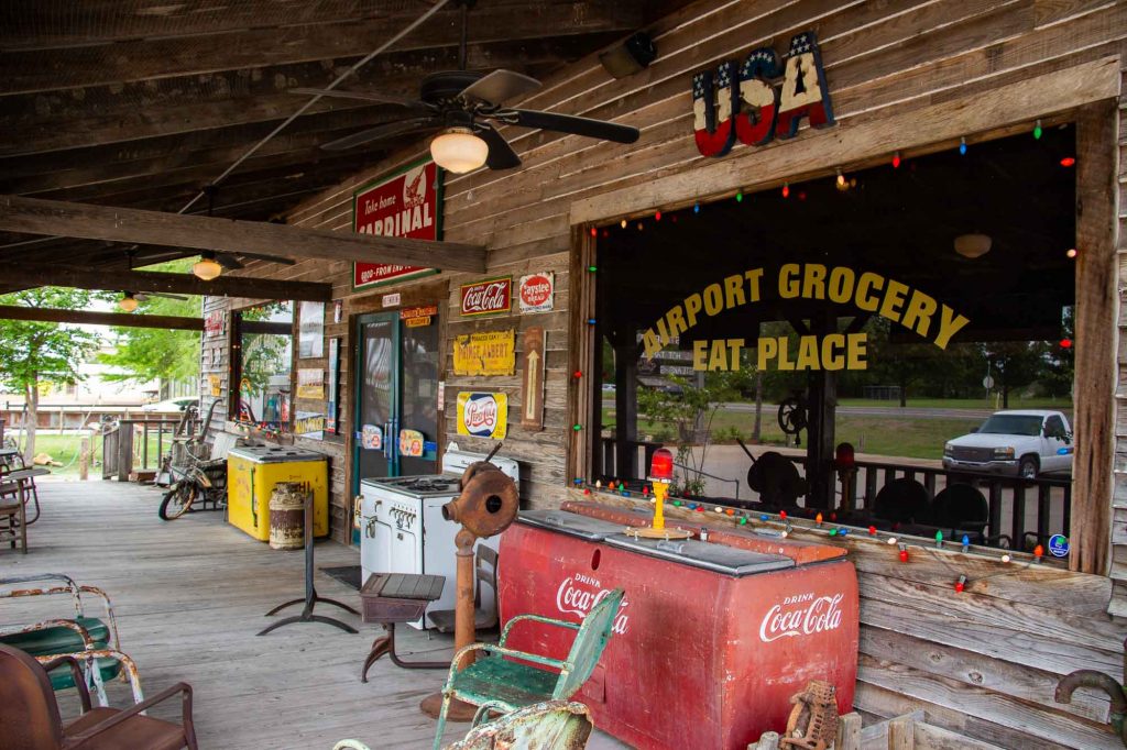 The front porch of the Southern restaurant Airport Grocery in Cleveland, Mississippi, with a vintage rocking chain, Coca-Cola cooler, and other Southern country style decorations. ©KettiWilhelm2022