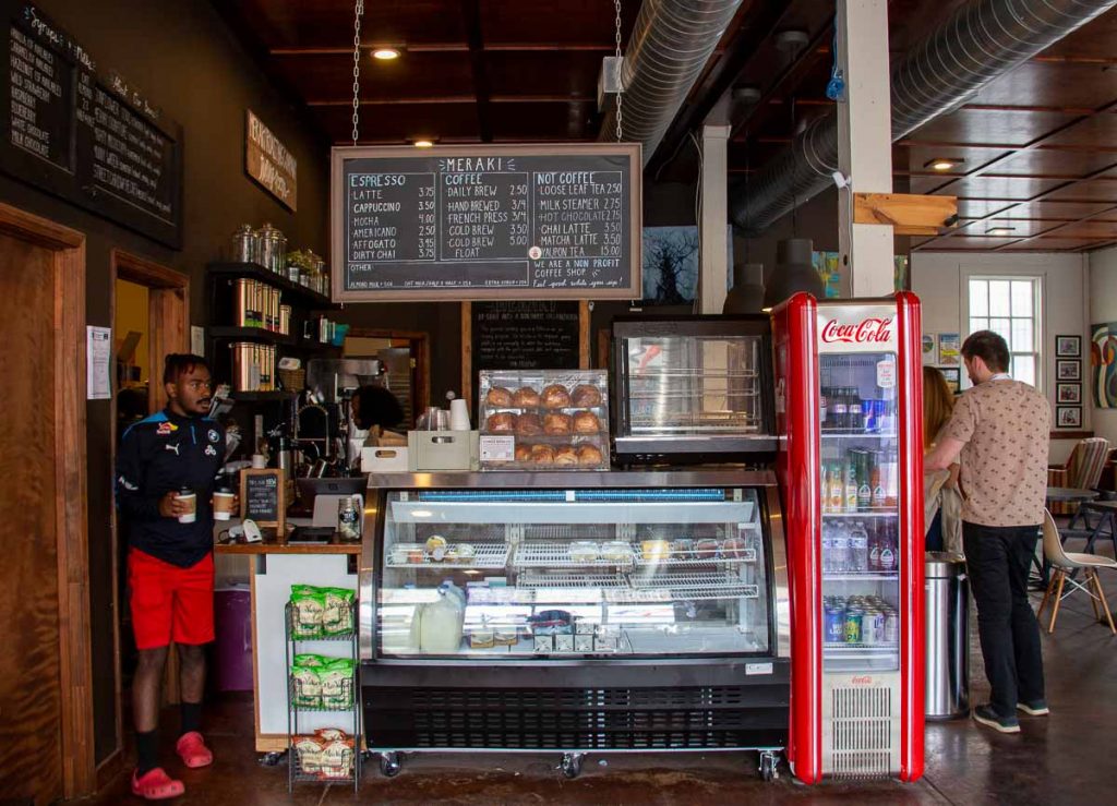 An employee dressed in red shorts and red Croc sandals carries two drinks out from behind the bar at Meraki Roasting Co, a local coffee roastery in Clarksdale that supports the community through a job training program. ©KettiWilhelm2022