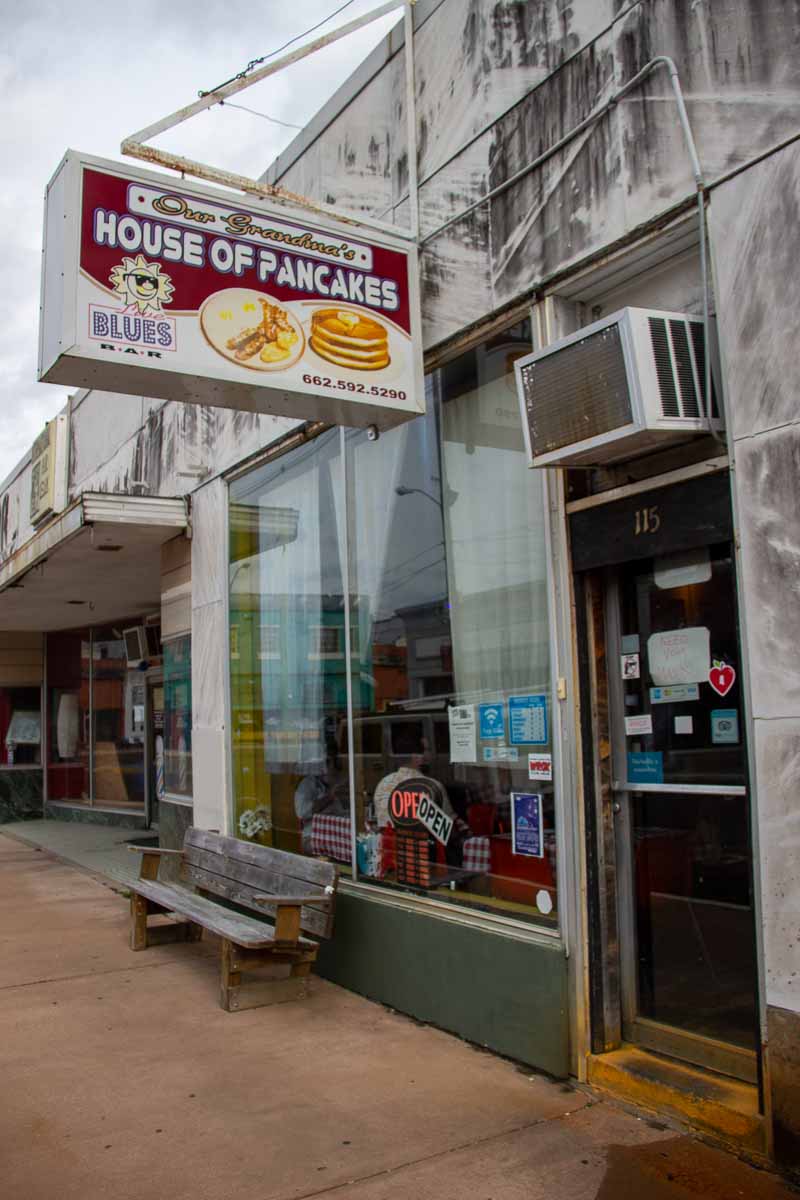 The outside of Our Grandma's House of Pancakes in Clarksdale, MS – an old sign with a picture of pancakes, and a white building with chipped paint. ©KettiWilhelm2022