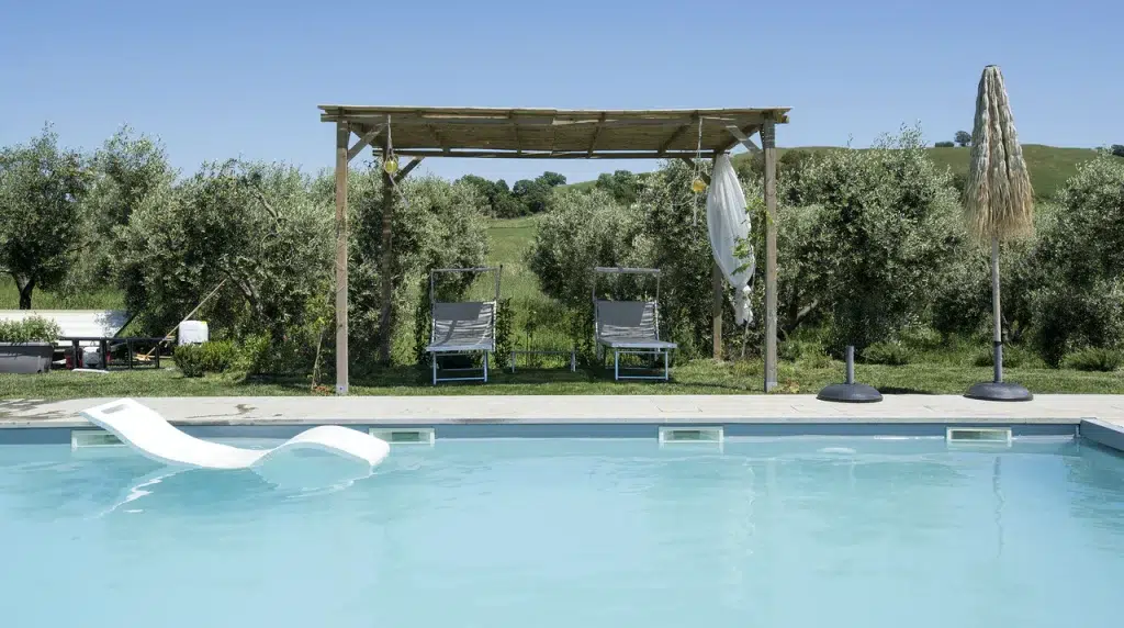 The pool at a sustainable villa in Tuscany, Italy, with a veranda and views of the Tuscan hills beyond the pool. The property is bookable through the AirBnb alternative platform Plum Guide.