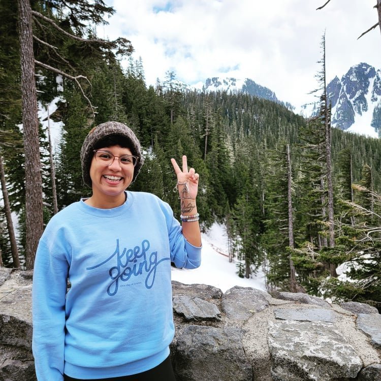 Keysha, a homestay host in Denver through the Couchsurfing alternative platform HerHouse, smiling and throwing up a peace sign in the mountains.