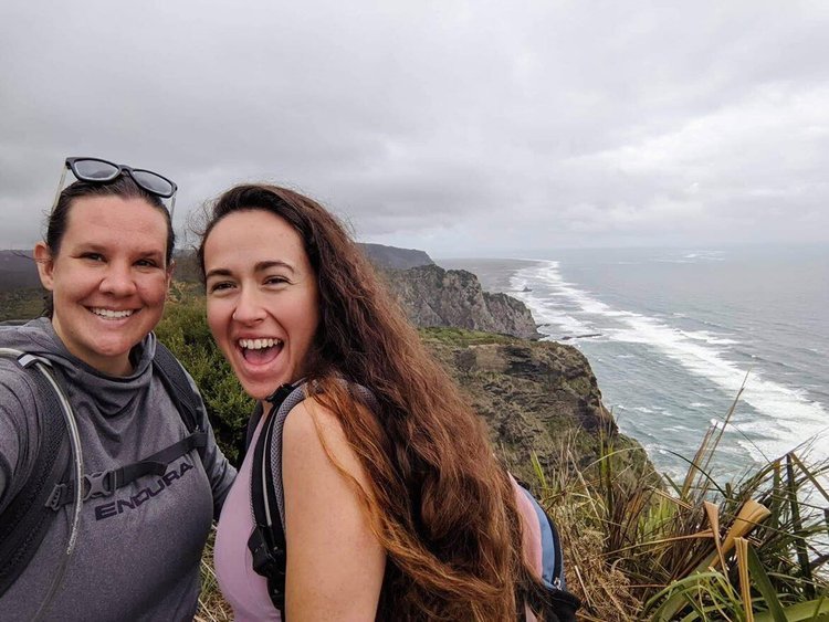 Two female members of the Couchsurfing alternative HerHouse smiling for the camera in front of a rocky coastline.