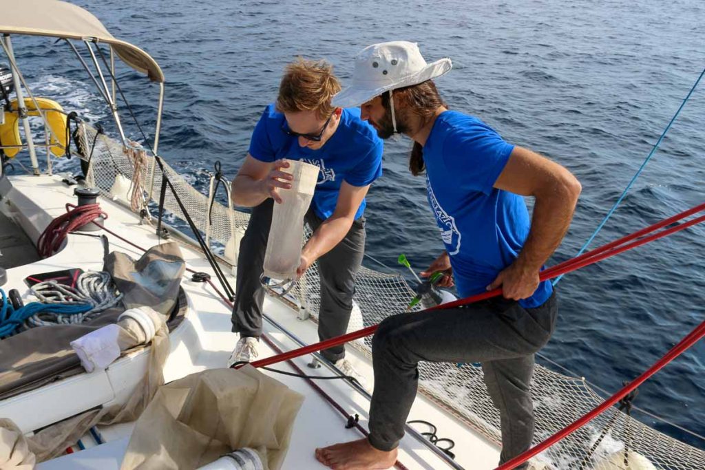 Two researchers on a sailboat, looking into the filter of a trawler that has just collected a water sample that will be tested for microplastics. ©KettiWilhelm2022
