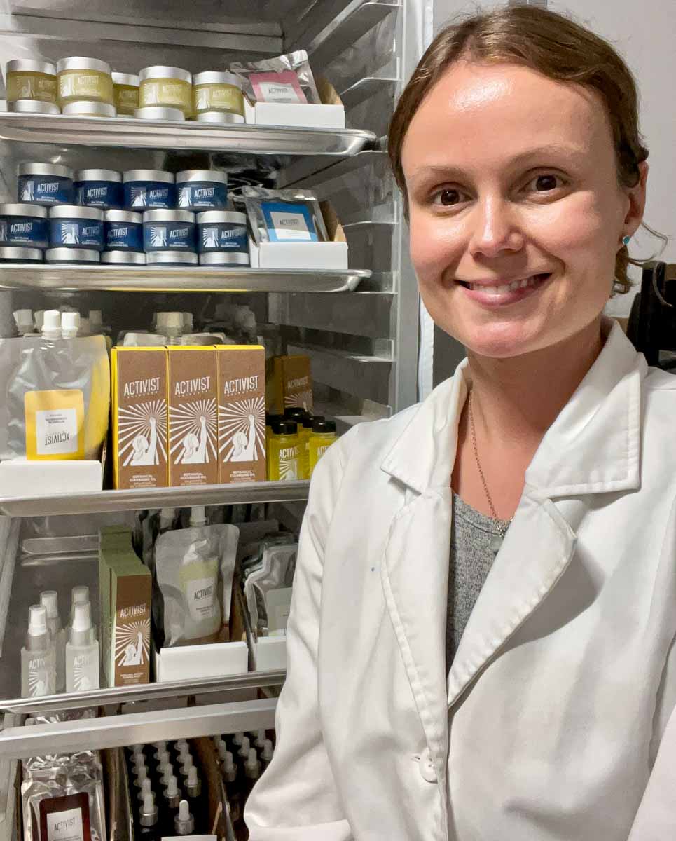 Activist Skincare founder Allison Callaway in a white lab coat in the studio where her small business makes eco-friendly skincare products.