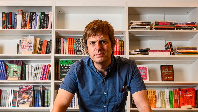 Bookshop.org (a sustainable, indie competitor to Amazon) founder Andy Hunter sitting in front of a bookshelf.