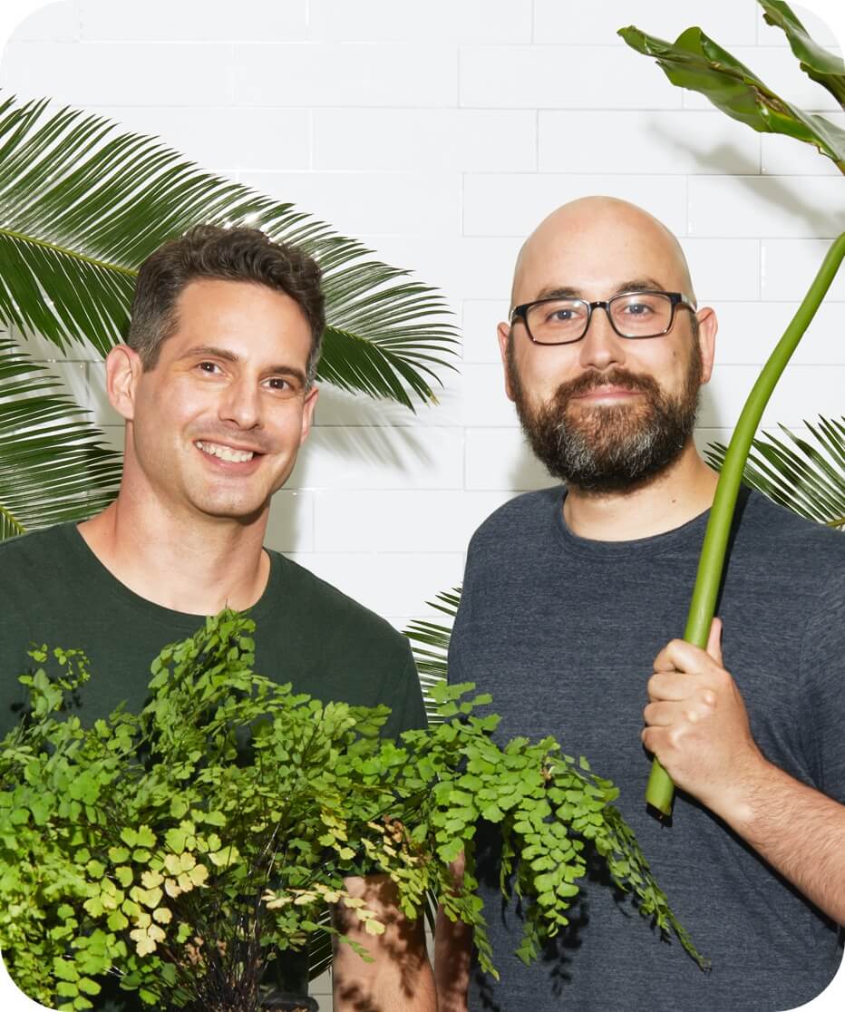 The two founders of Leaf Shave Co, a small business with a sustainability mission, posing in a jungle of houseplants. 