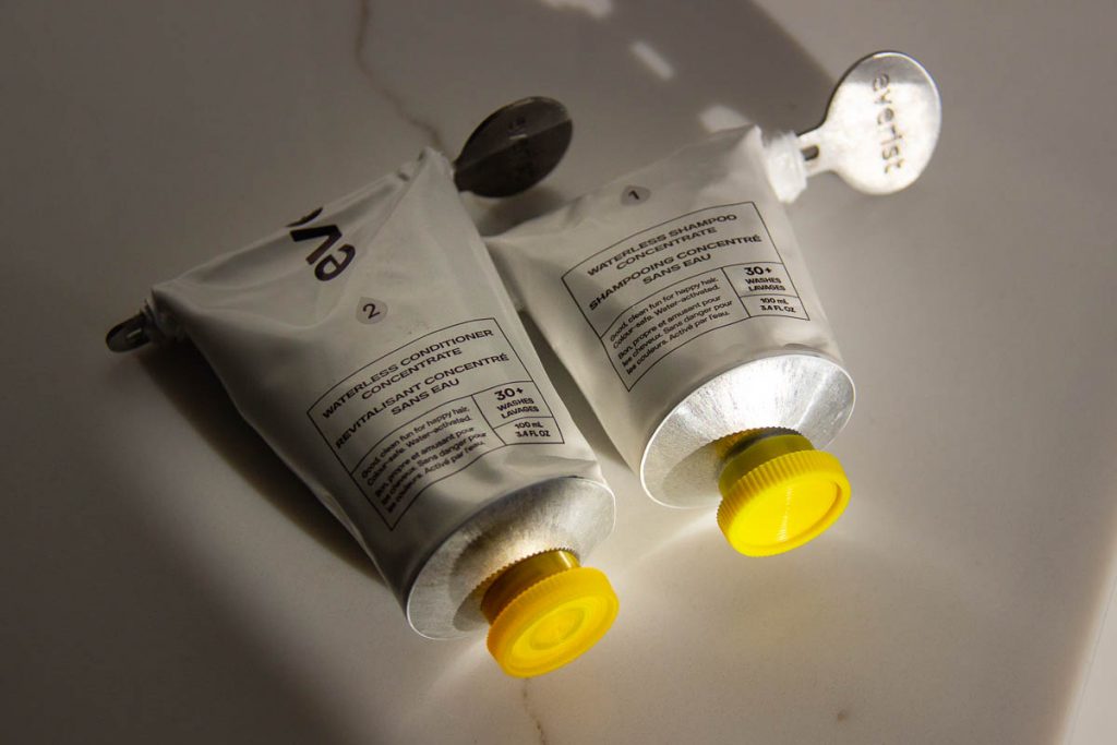 Aluminum tubes of concentrated, plastic-free Everist shampoo and conditioner sitting on a white marble counter top. Their caps are both very similar shades of yellow. ©KettiWilhelm2022