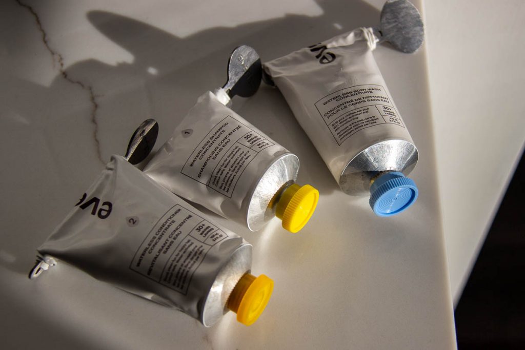 White aluminum tubes of plastic-free, concentrated Everist shampoo, body wash, and conditioner sitting on a white marble counter top. ©KettiWilhelm2022