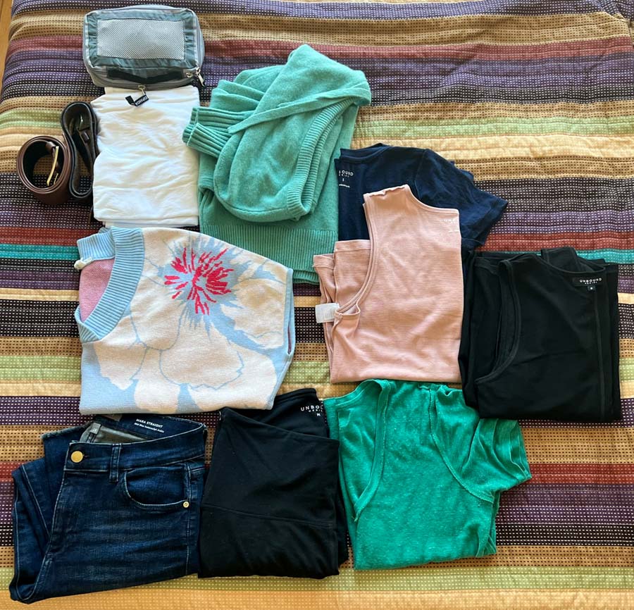 A travel wardrobe spread out on a bed, mostly comprised of merino wool items from this review of Unbound Merino. ©KettiWilhelm2022