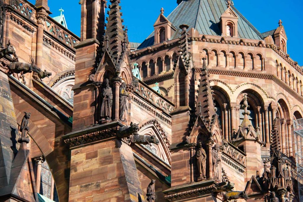 Architectural details on the famous Strasbourg Cathedral show gargoyles and other figures carved out of stone shades of red and orange, against a blue sky. ©KettiWilhelm2023