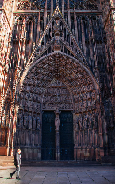 A man walks in front of the facade and main doors of the Strasbourg Cathedral. ©KettiWilhelm2023