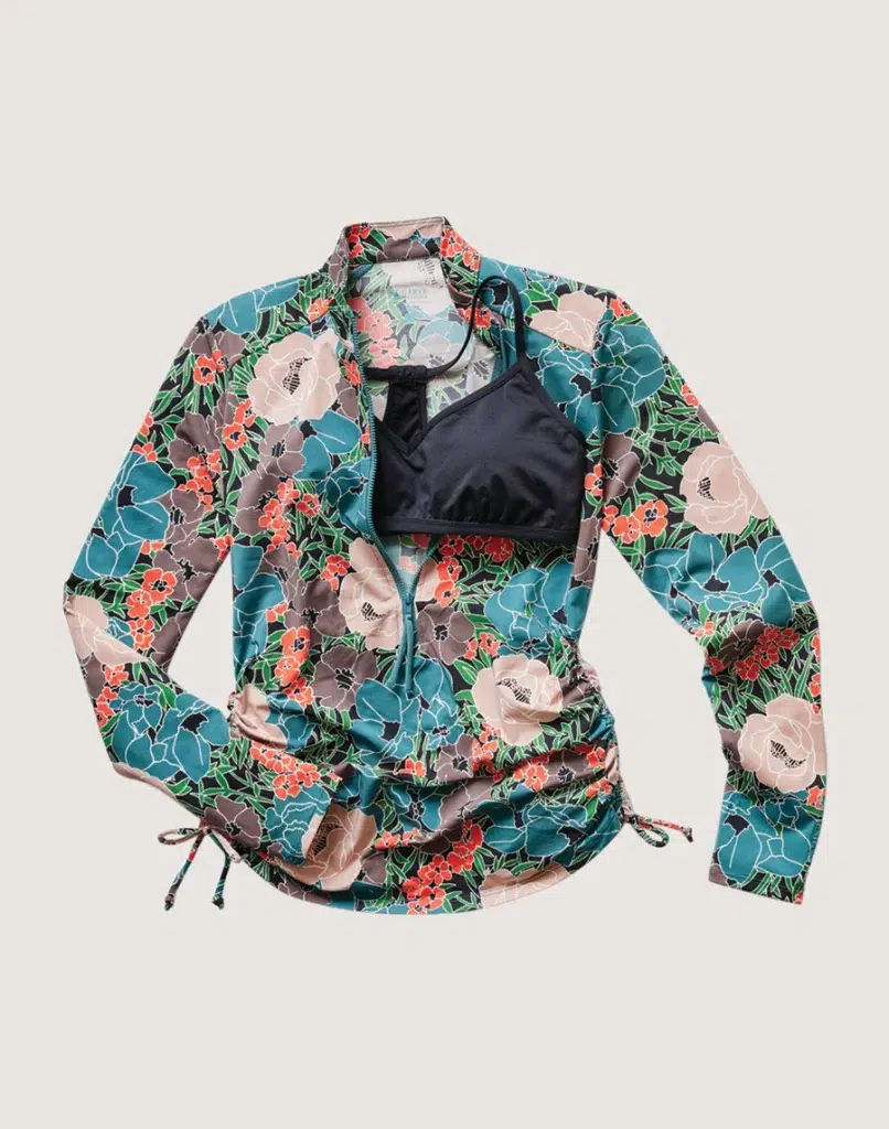 A floral-printed, zip-up rash guard from Carve Designs, shown with a black sporty bikini top underneath. Both are top items on this Baja packing list.