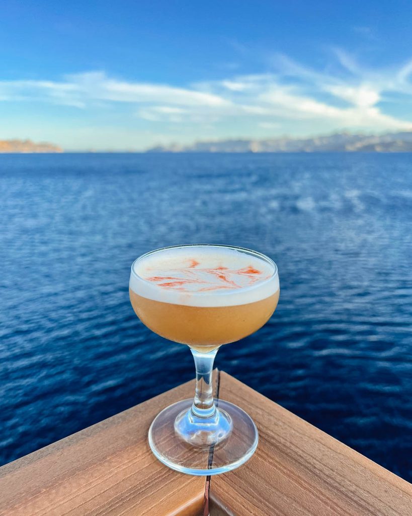 A cocktail sitting on the railing of the UnCruise ship, with the bright blue Sea of Cortez behind. ©KettiWilhelm2023