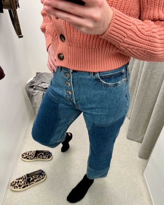 The dressing room mirror selfie of the author trying on sustainable clothing items from Everlane – a pair of jeans with dramatic patches on the thighs and a salmon-colored button-up cardigan. ©KettiWilhelm2023