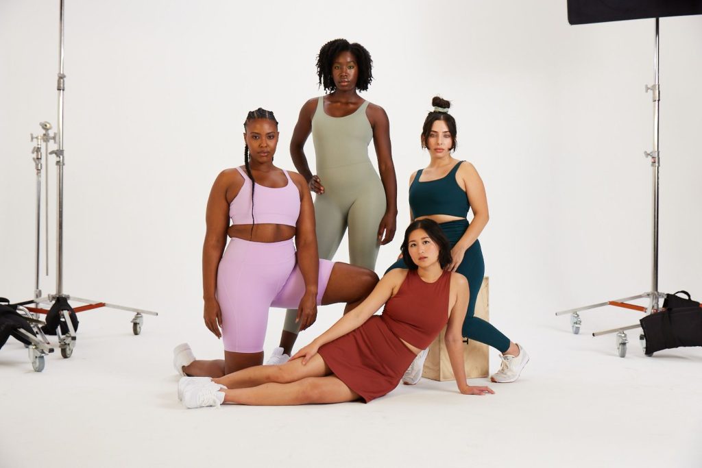 Four women of different races and body types model different styles and colors of sustainable clothing made from recycled water bottles, from Girlfriend Collective.