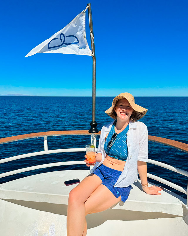 Ketti, the travel writer and author of this UnCruise review, sitting on the deck of the Safari Voyager ship, smiling with a cocktail in hand. ©KettiWilhelm2023