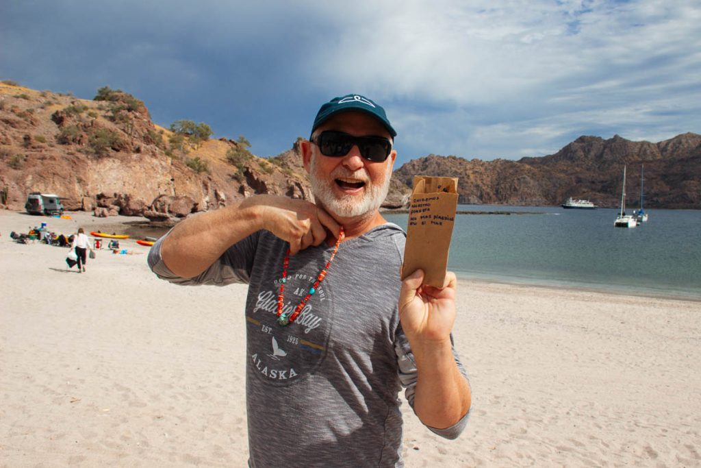 The CEO and owner of UnCruise, Dan Blanchard, on the beach in Baja California, holding up a coral necklace made by a local family, along with its packaging – a paper bag with a hand written message in Spanish: “Let’s take care of our planet. No more plastics in the sea.”©KettiWilhelm2023