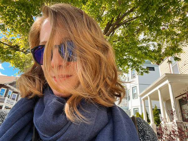 A selfie I snapped while walking down the street on a sunny day, with a the green leaves of a tree overhead, after washing my wavy, blond hair with Viori products. ©KettiWilhelm2023