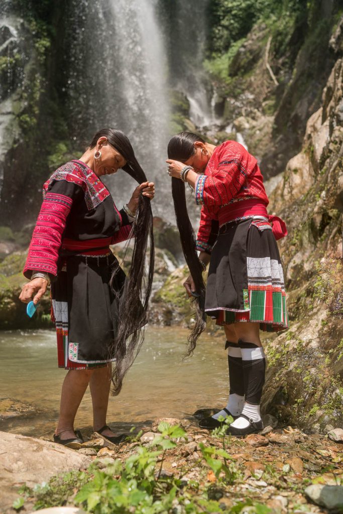 Women of the Red Yao tribe, who work with the Viori shampoo bar brand, washing their long hair in front of a waterfall.
