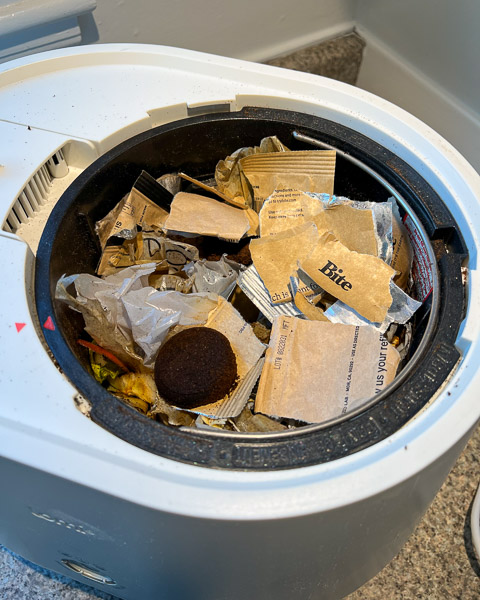 Compostable packaging from Bite Toothpaste Bits ripped up into approximately 3-inch pieces, inside the Lomi countertop composter. ©KettiWilhelm2023